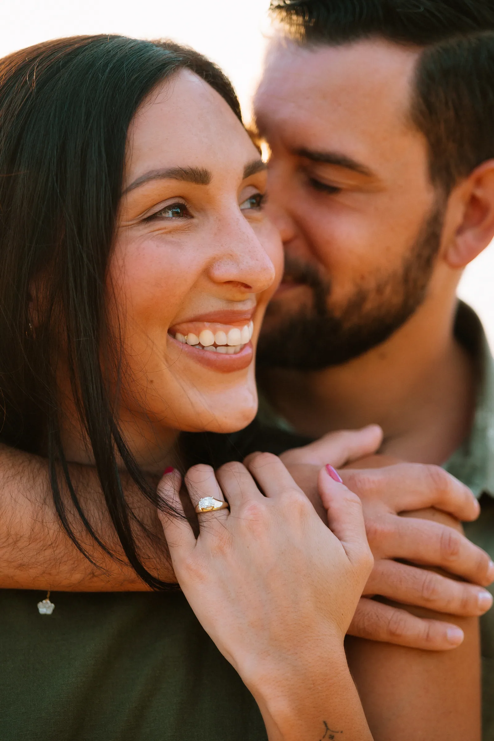 A close portrait of a couple laughing, her ring hand resting on his shoulder