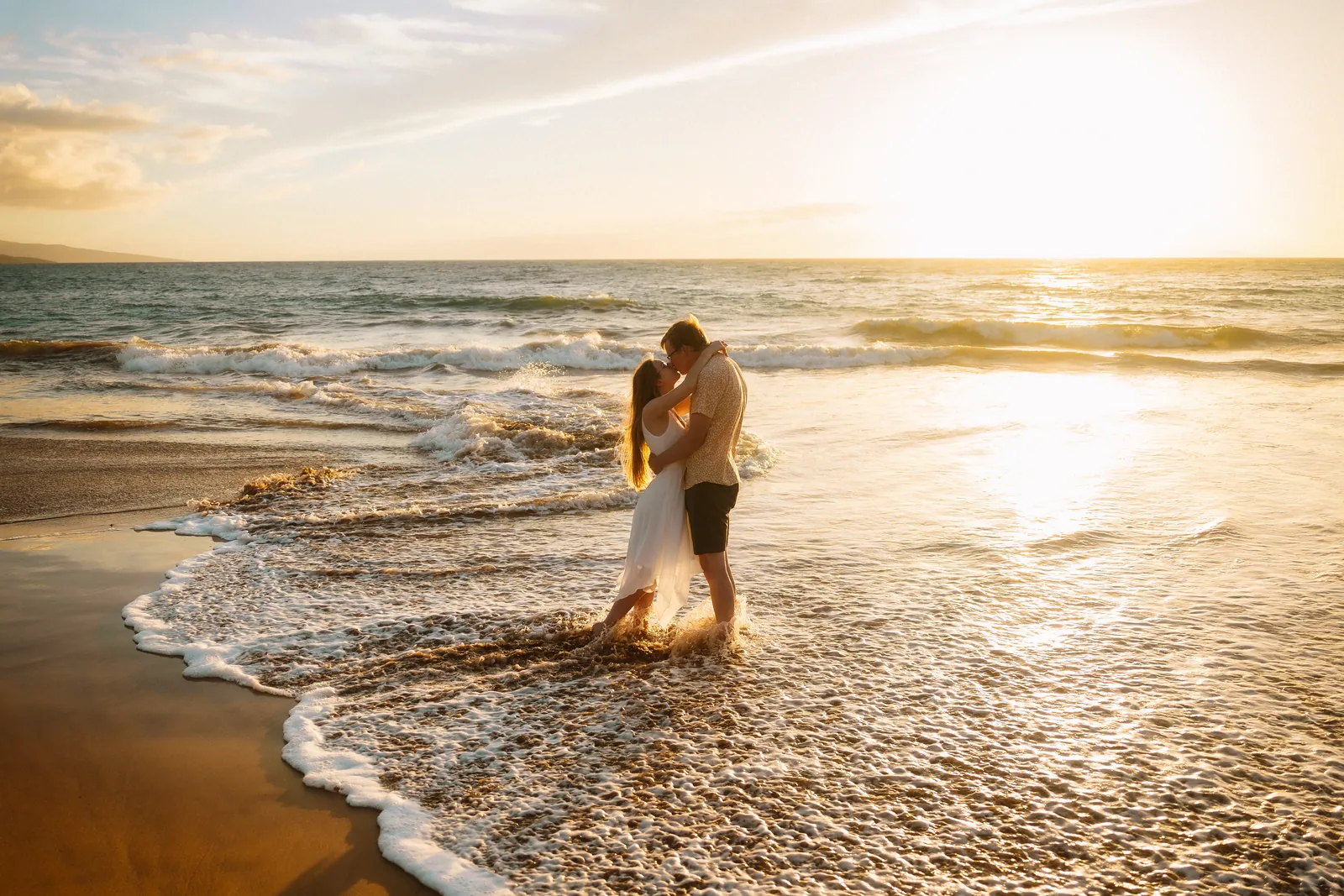 A couple embracing in the shallows with the sun's path running out to sea