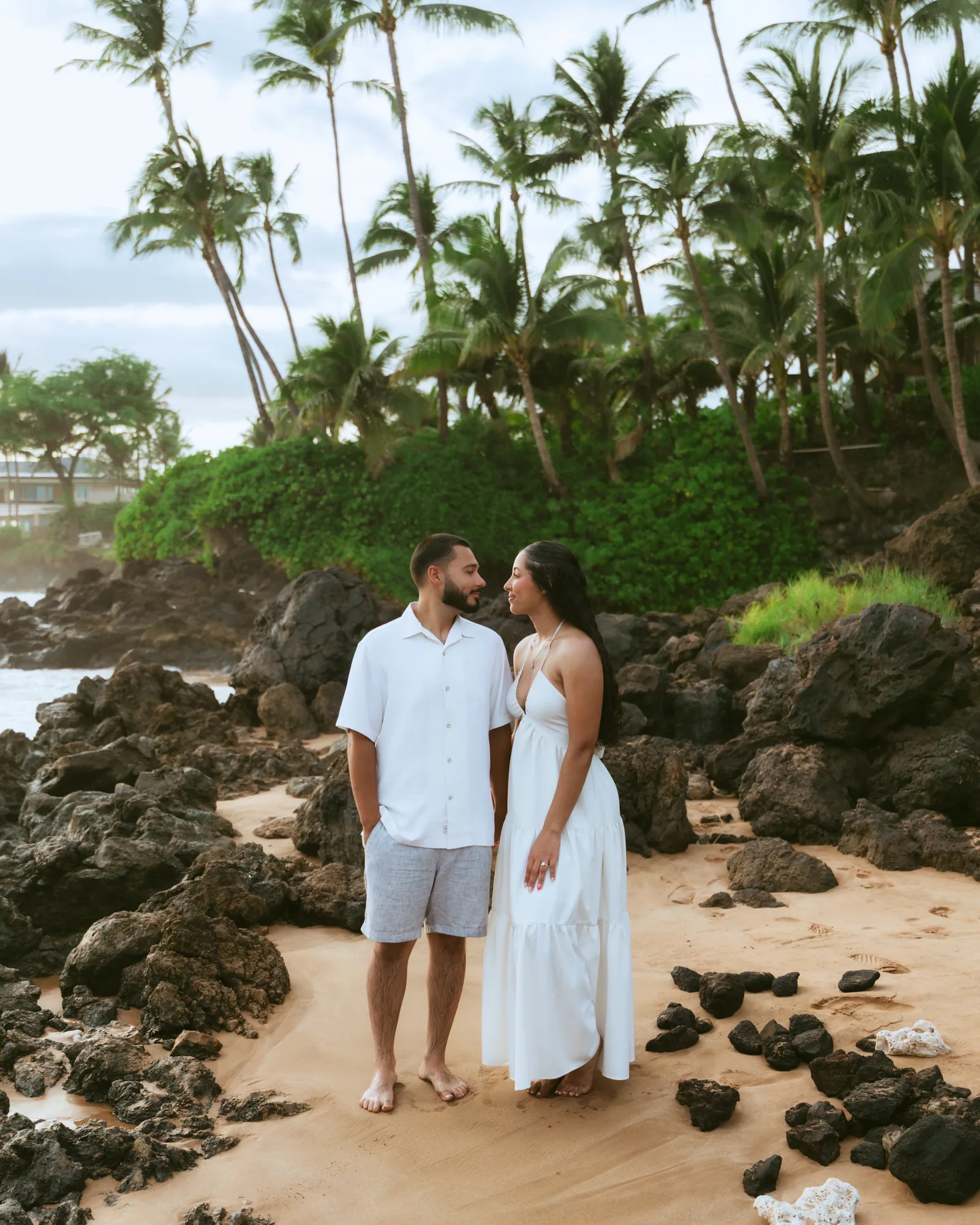 A couple in white standing together among lava rocks on the sand