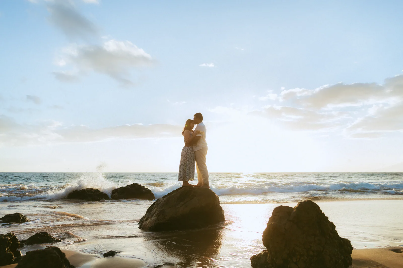 A couple embracing on a rock offshore, silhouetted against the sky