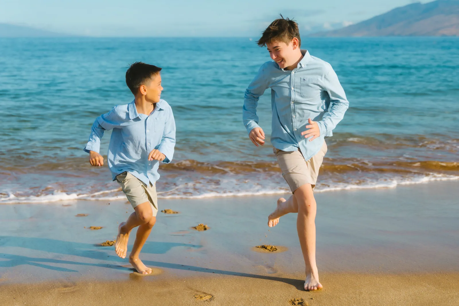 Two brothers running through the shorebreak, laughing