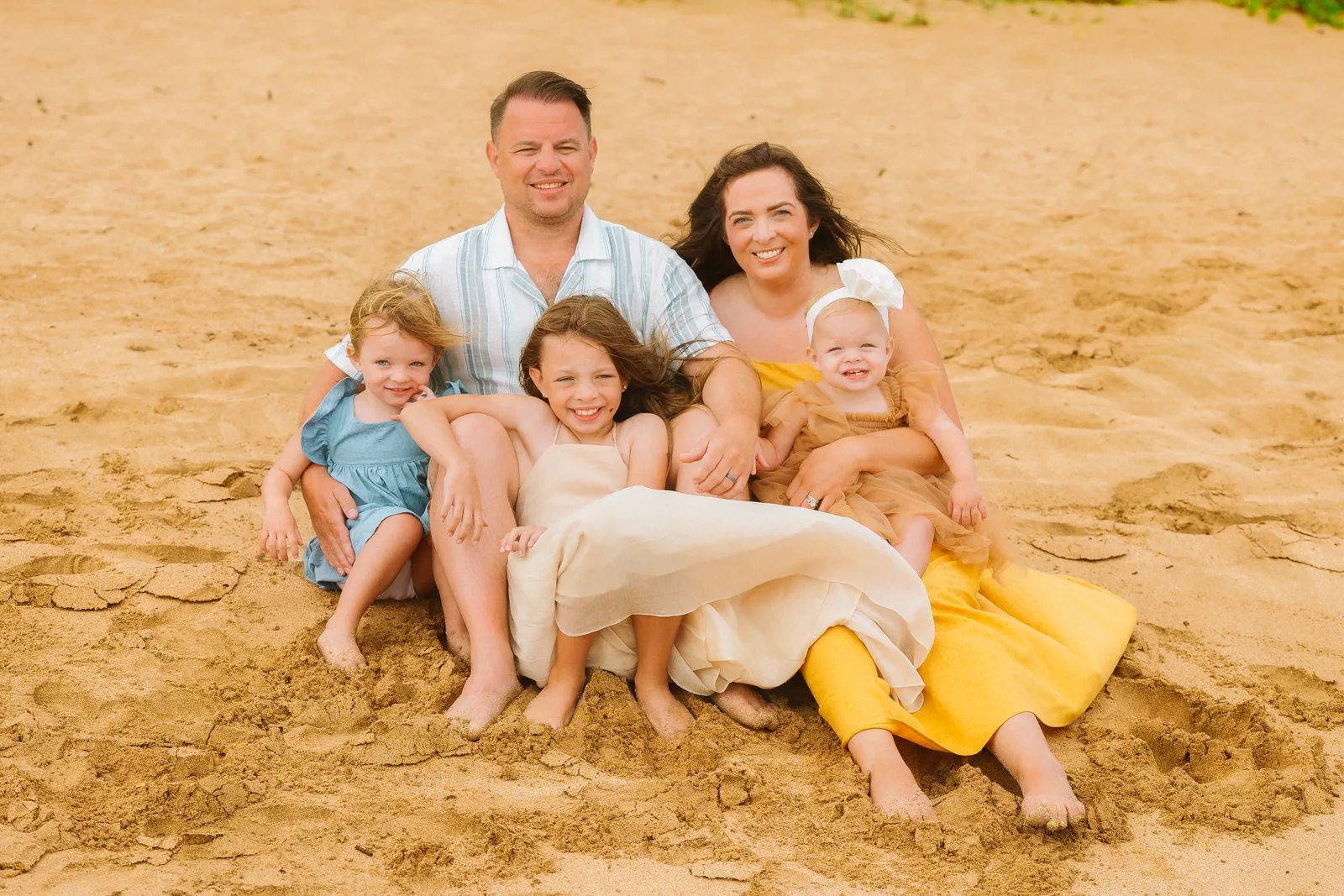 A family sitting together in the sand, the children piled across their parents