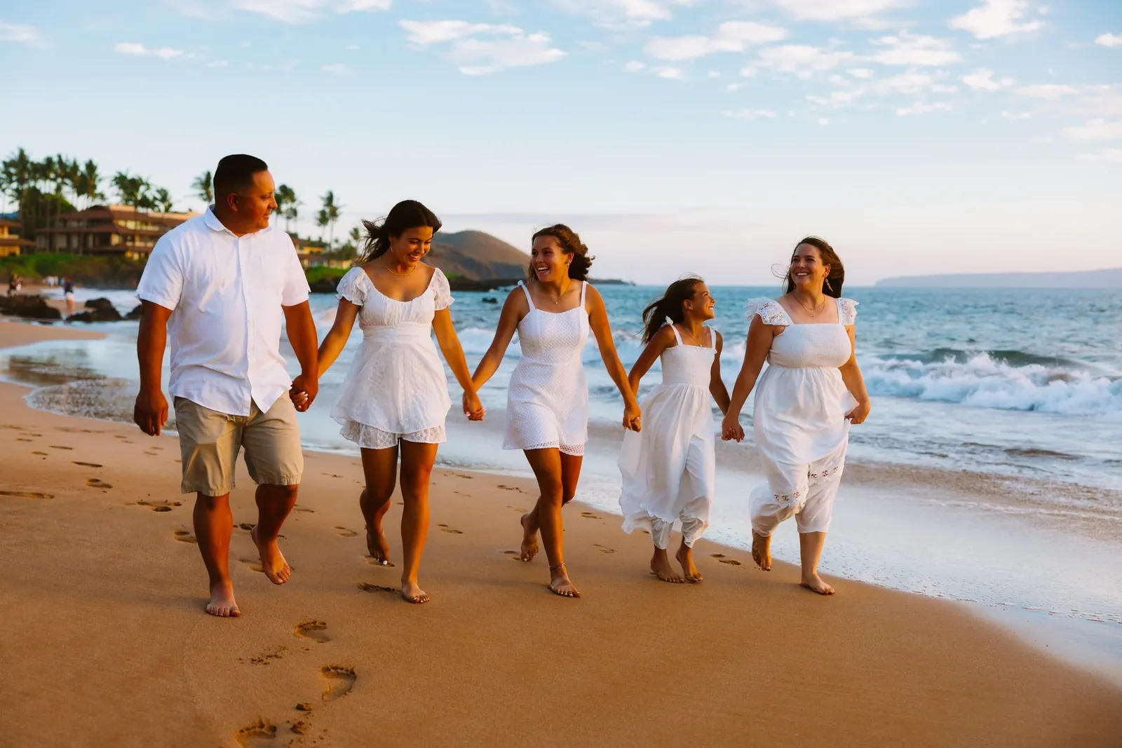 Family in white walking the shoreline together beneath the palms on Maui