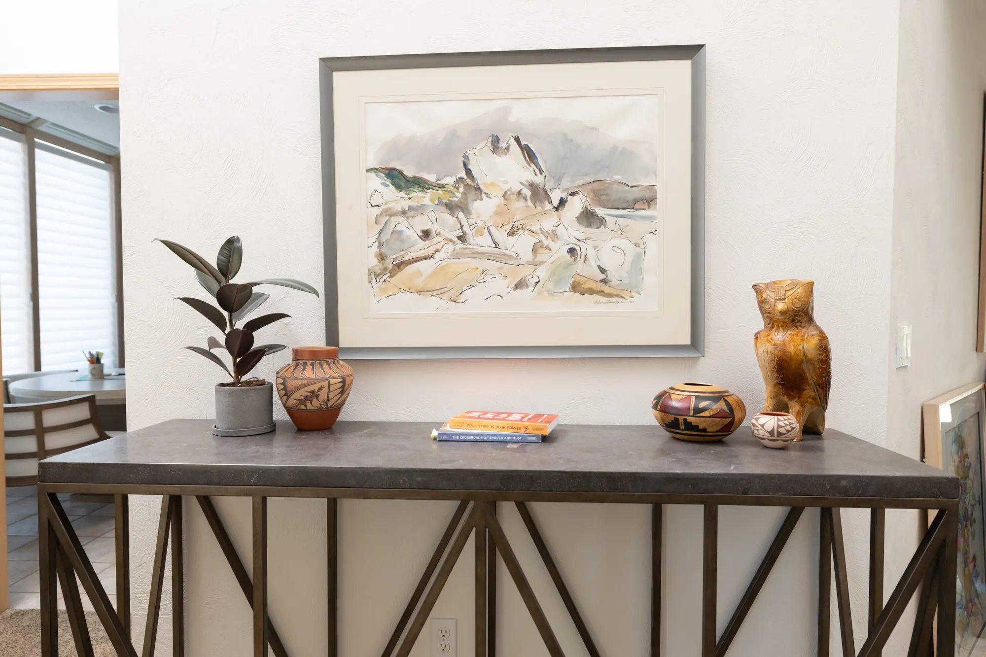 A dining room console styled with framed art, pottery and greenery