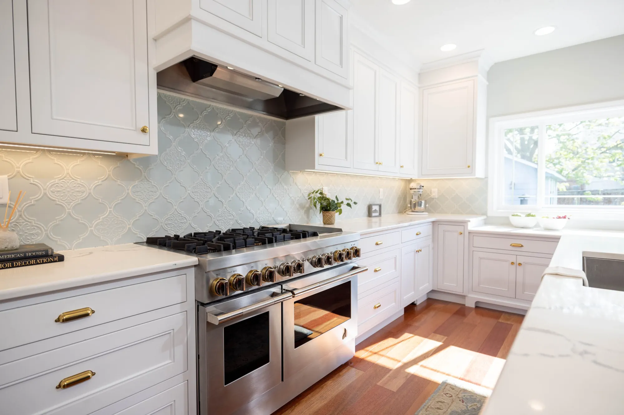 A Kalluna-designed kitchen with light cabinetry, a tile backsplash, warm wood flooring and a professional range