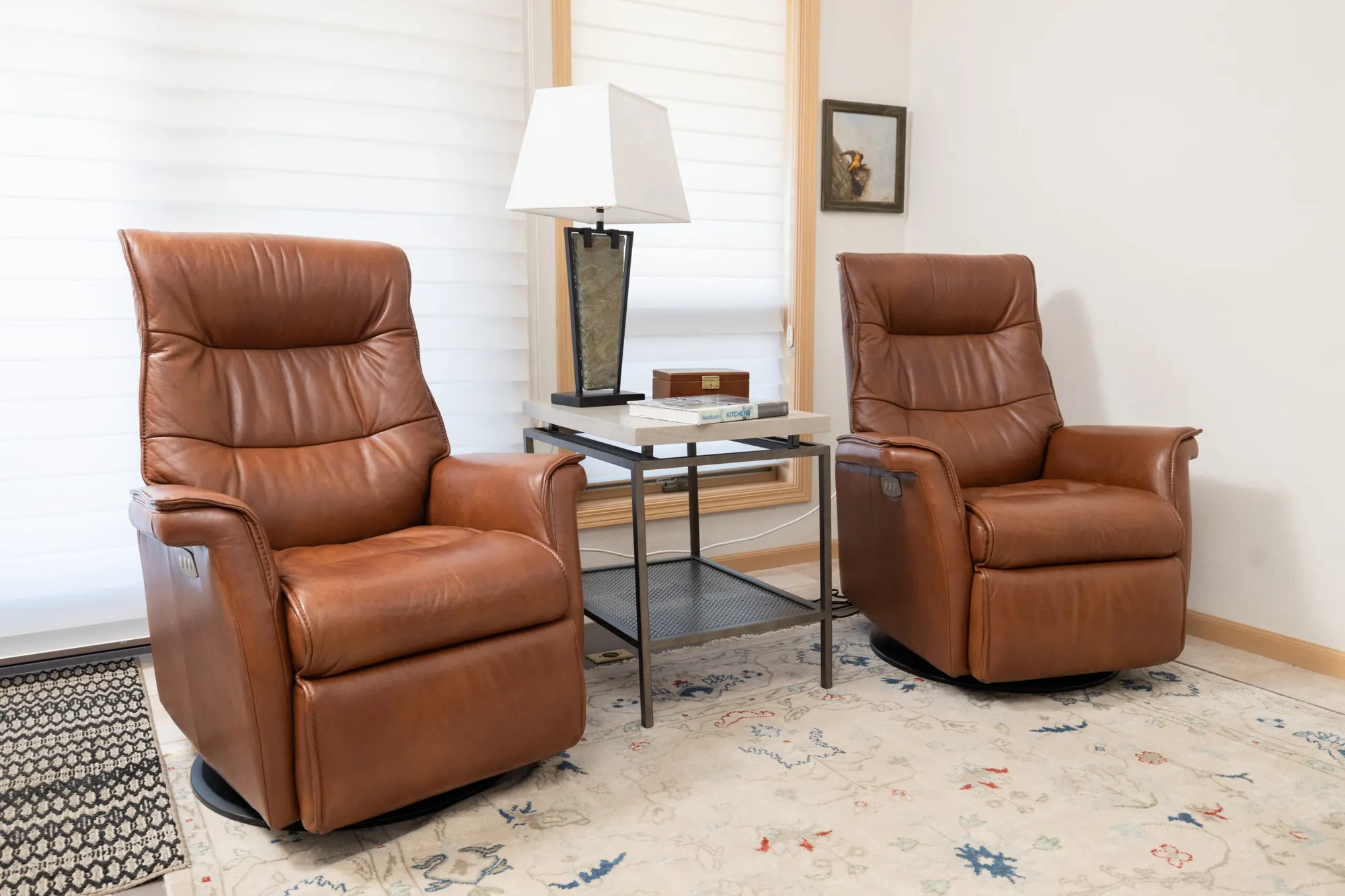 A living room with paired leather recliners, a side table and a layered rug